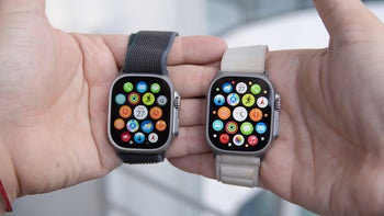 A close-up of a man holding two Apple Watch Ultra smartwatches next to each other.