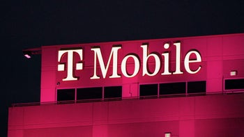 A sign with the T-Mobile wordmark sits atop an office building surrounded by lights at night.